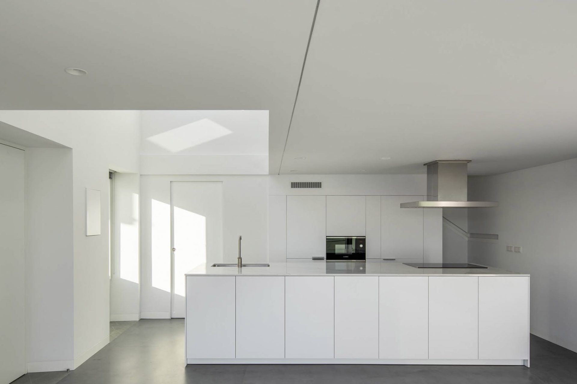 Large open-plan white kitchen inspiration with minimalist island and facades without handles