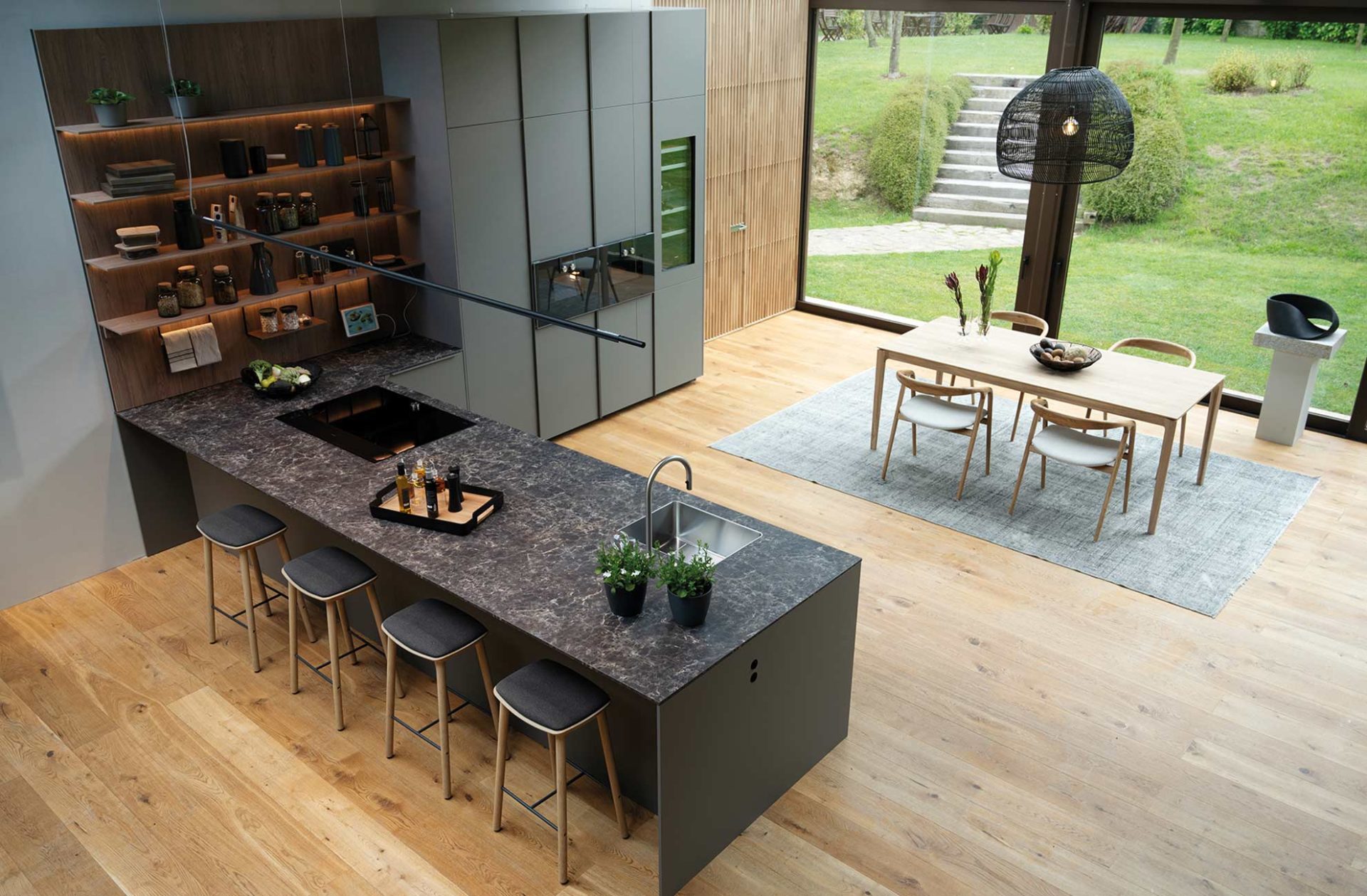Large peninsula kitchen-dining room overlooking a garden. Grey breakfast bar with anthracite marble countertop, stove and sink.