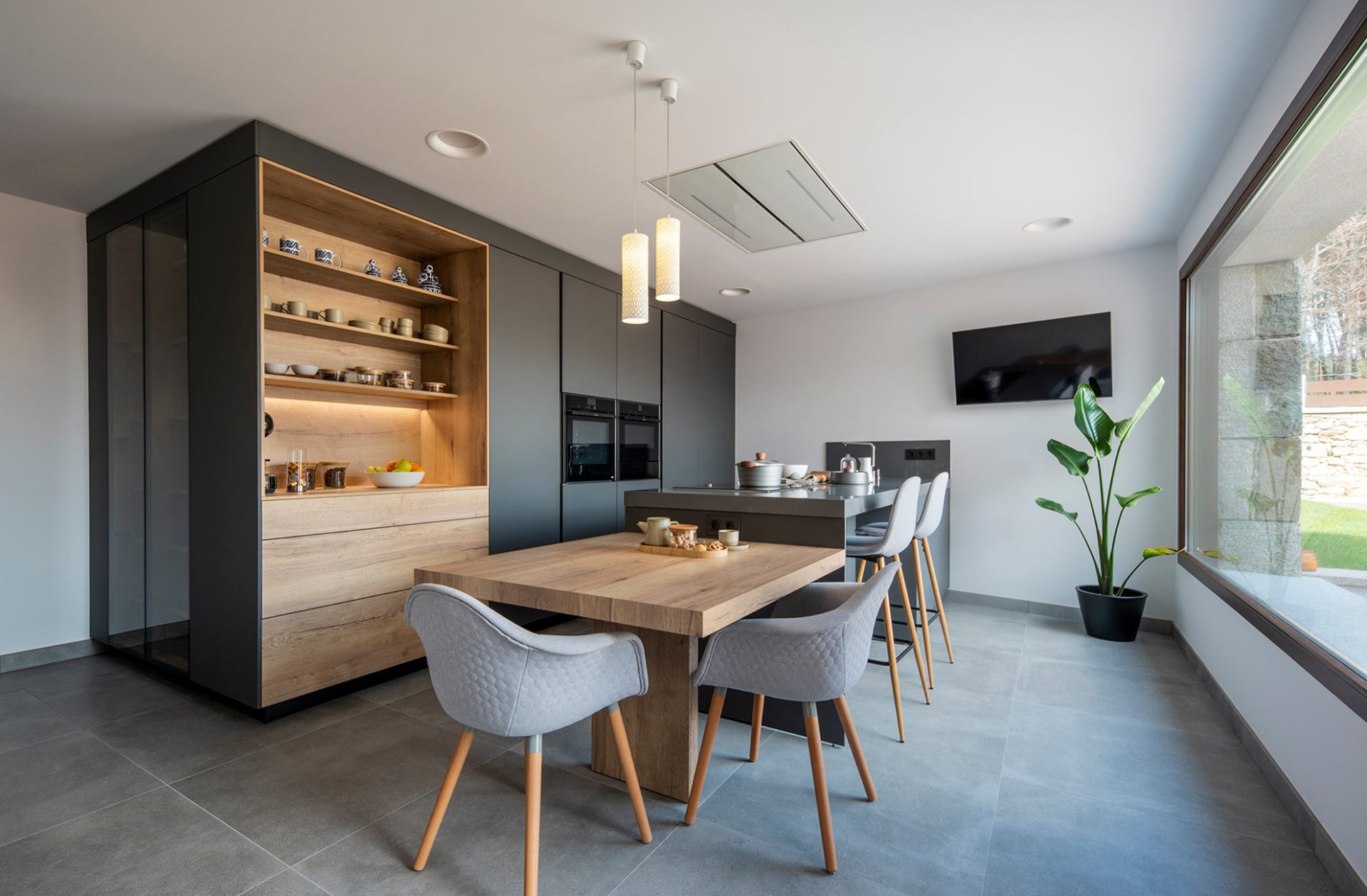 Galley kitchen-dining room in grey hues, with a peninsula integrating a breakfast bar and a wooden table attached.