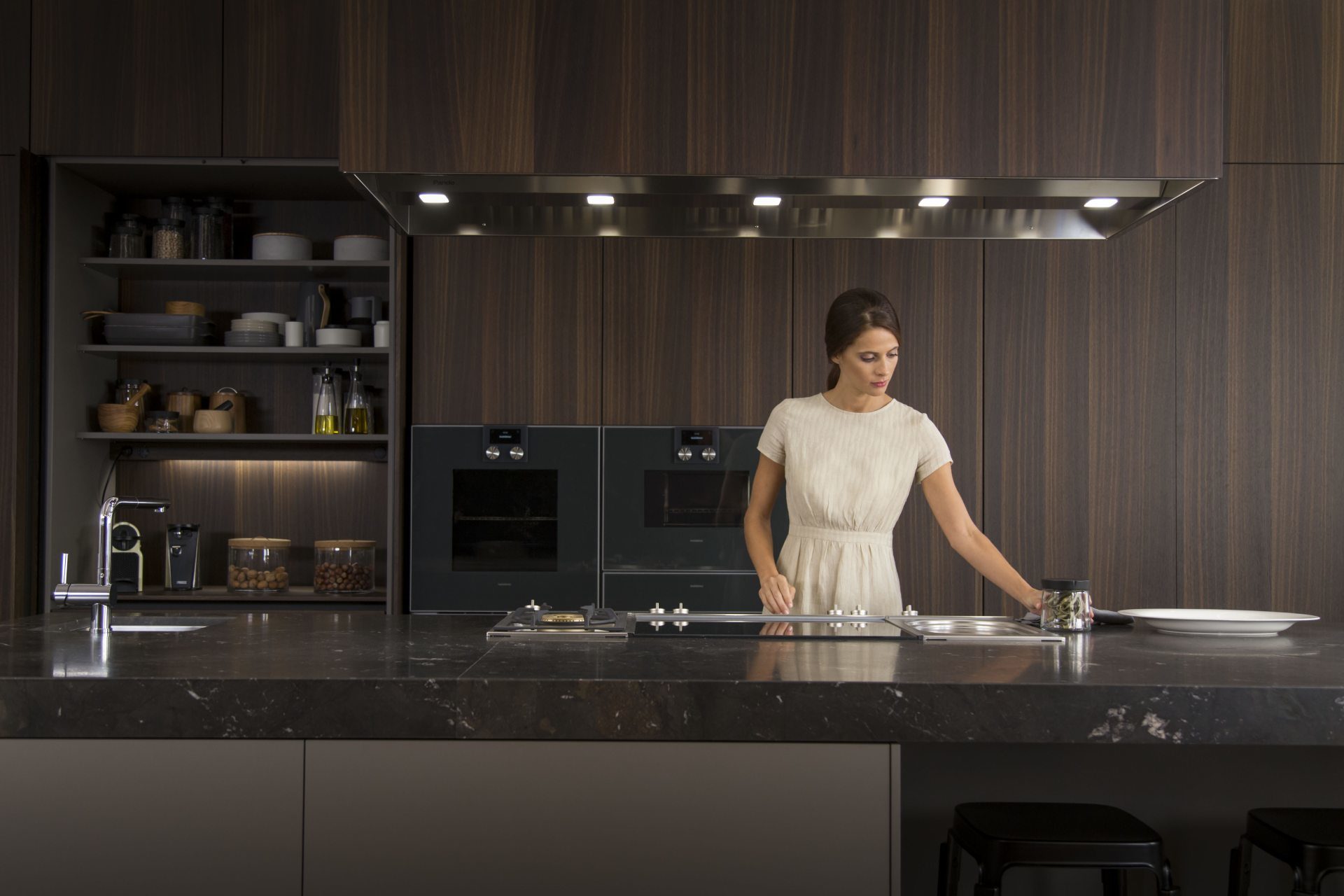 Photo of a woman in a Smoked Oak veneer kitchen with central island and extractor hood