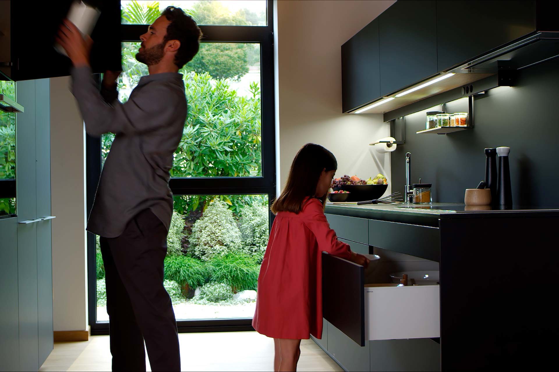 A man and a little girl in a black open kitchen with a parallel layout