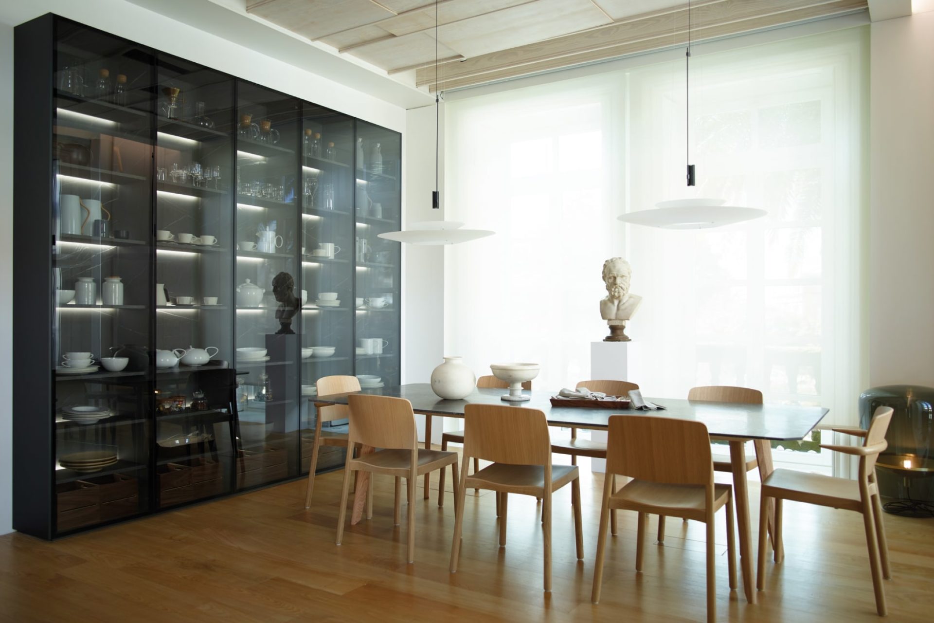 Dining room with wooden table and chairs, a black cupboard with a smoked glass front, pendant lamps and a Balloon floor lamp