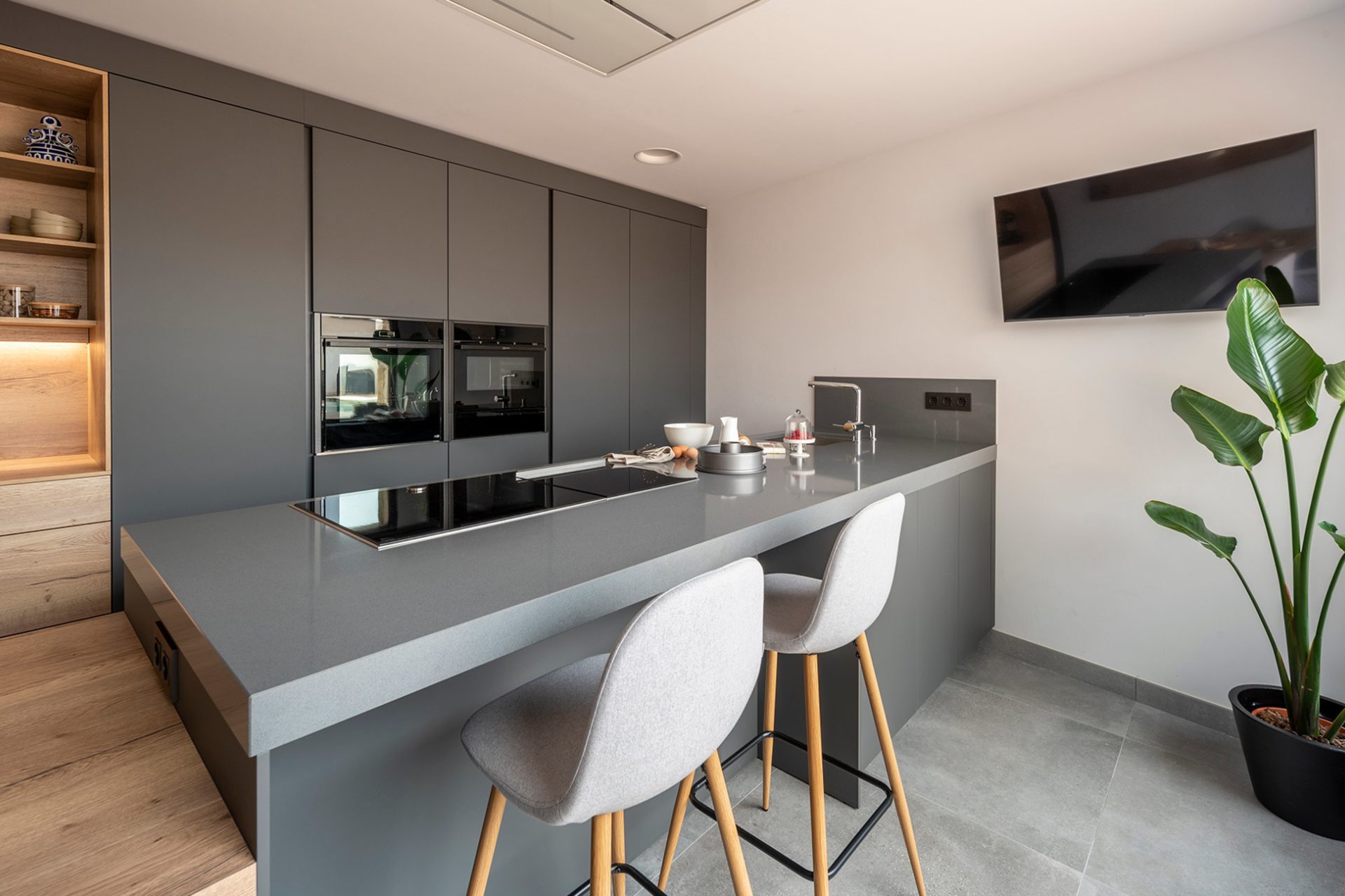 Anthracite, steel grey and wood peninsula kitchen with sink, stove, integrated breakfast bar and table attached.