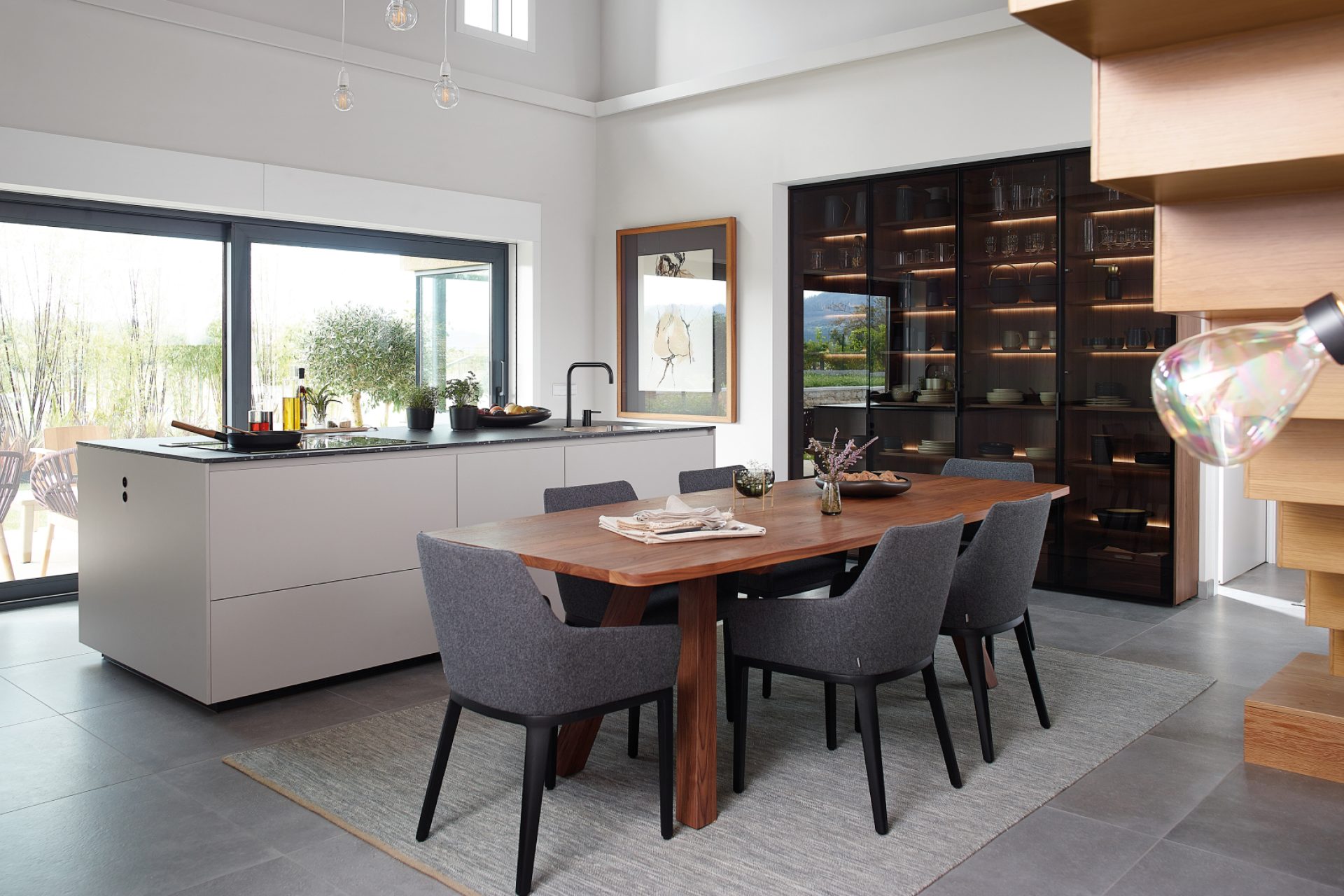 Îlot central de cuisine blanche ouverte sur salle à manger composée d'une table en bois et de chaise en tissu avec buffet vitré