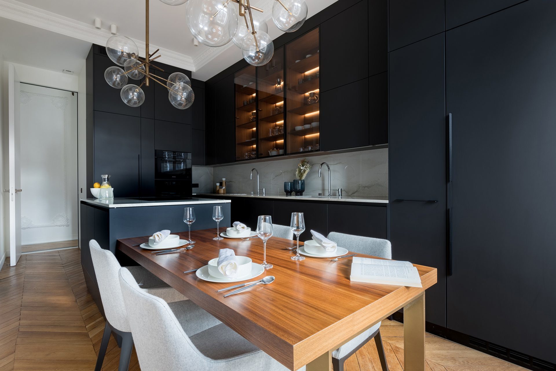 Image of black kitchen composed of column, tall and base units and a central island extended by a wooden table